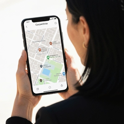 Personne utilisant un smartphone avec une carte de Carpentras affichée, indiquant des entreprises locales